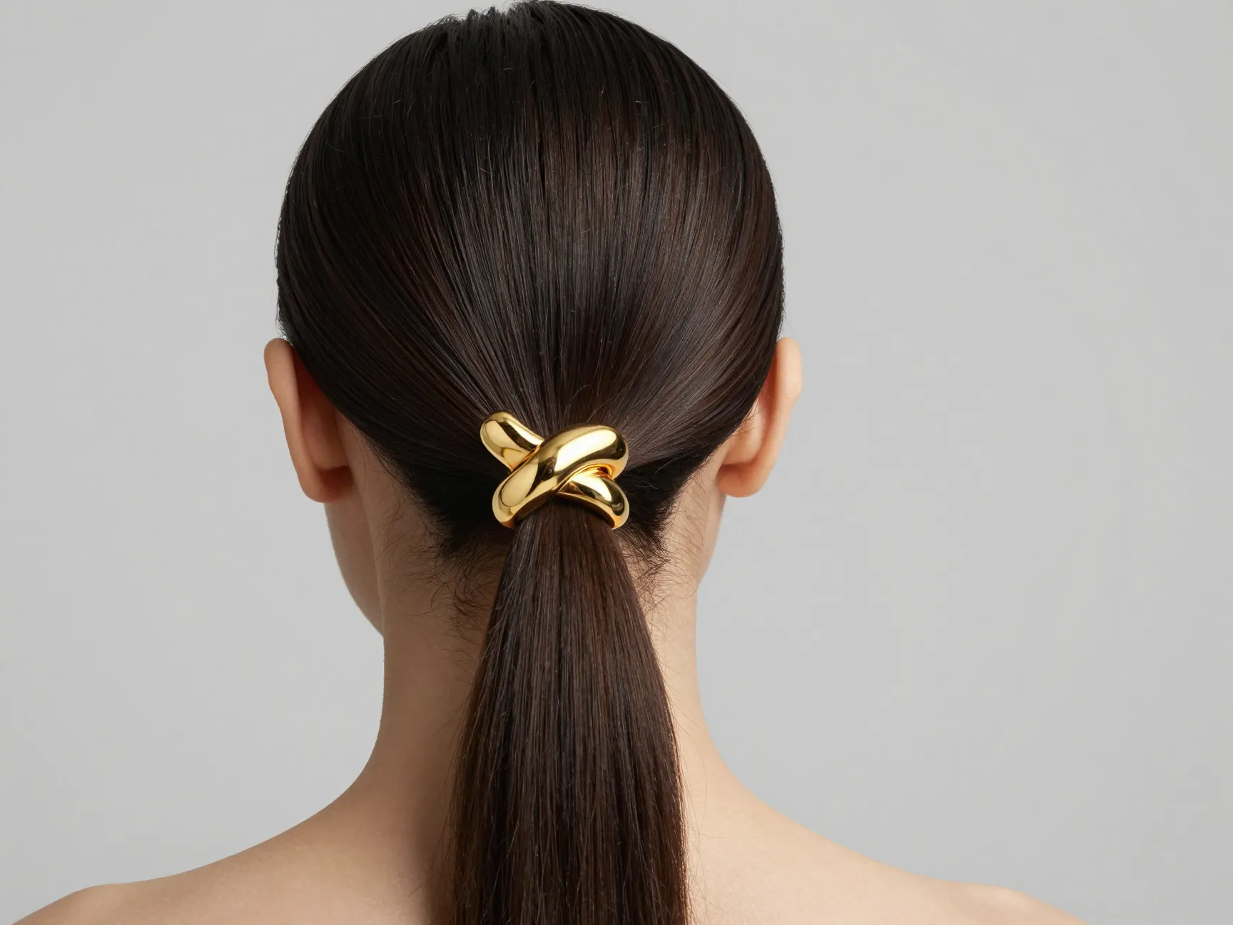Sleek low ponytail with sculptural gold statement cuff accessory