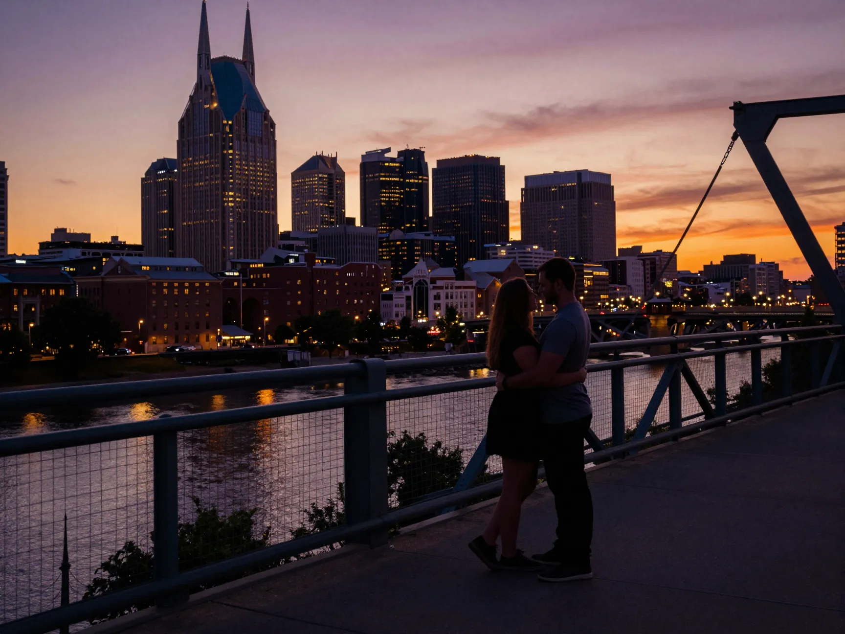 Couple embracing on pedestrian bridge at sunset with city skyline