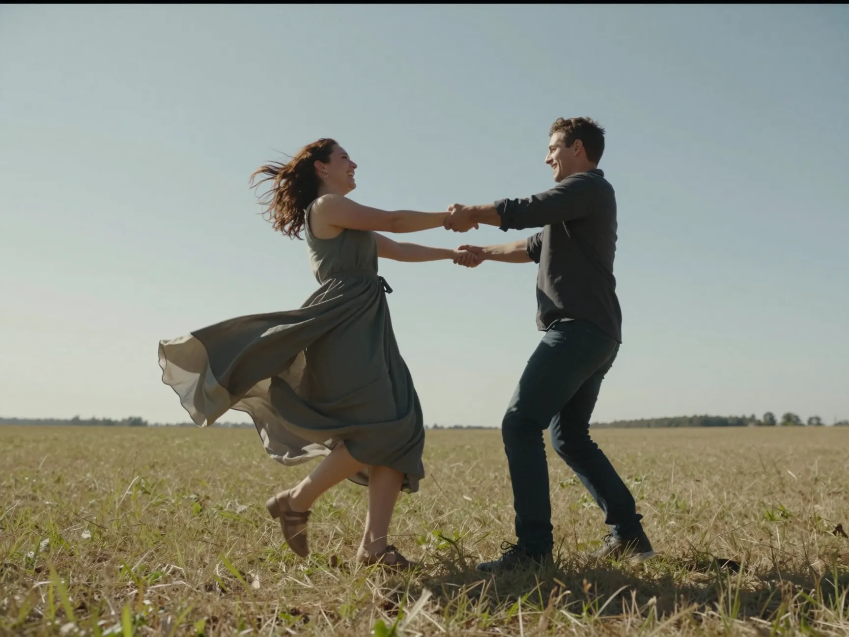 Woman in flowy dress being spun by partner in open field