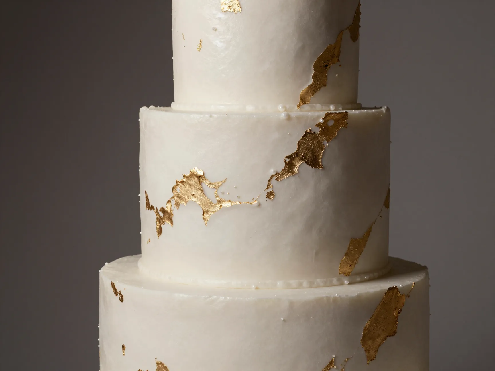 Luxurious pearlized fondant wedding cake with edible gold leaf
