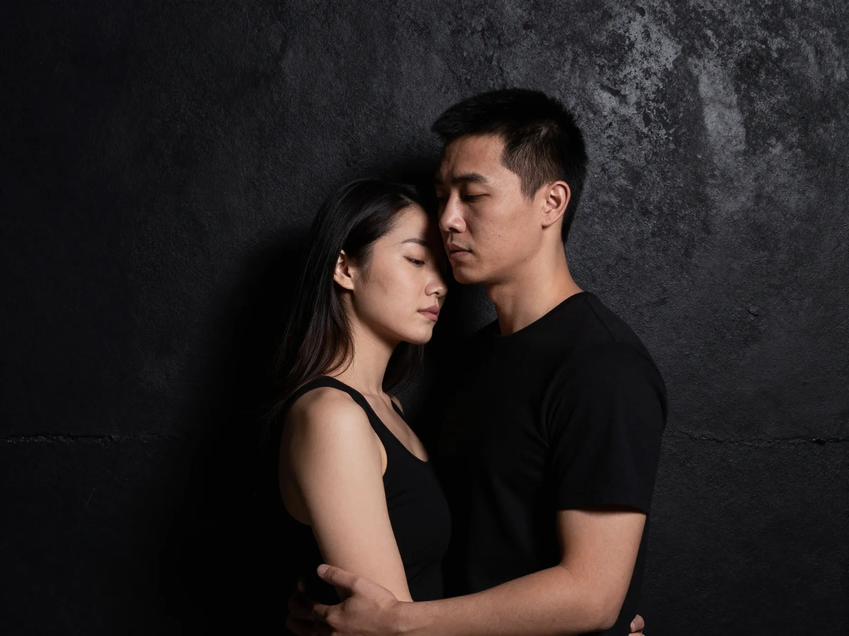 Couple dramatic split lighting black concrete wall