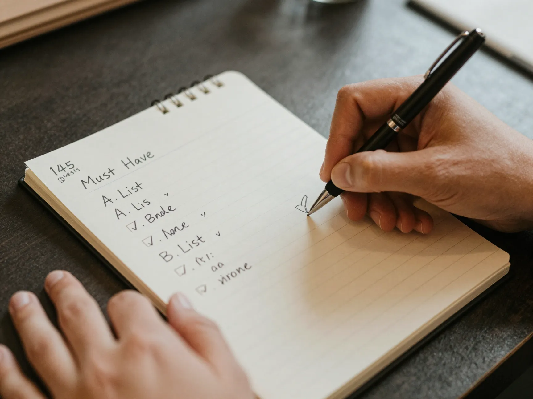 Draft wedding guest list on paper with pen and check marks