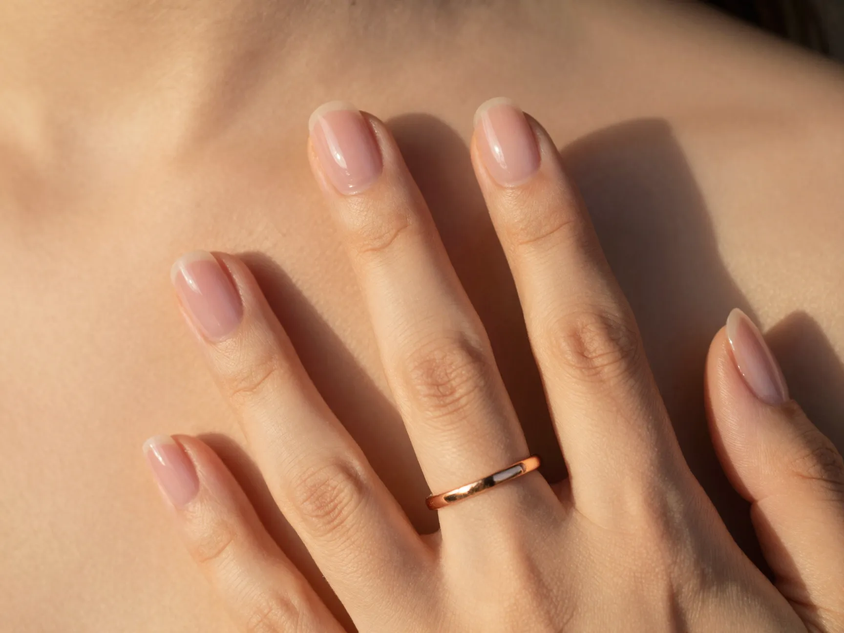 Translucent sheer pink nails with rose gold ring in warm light