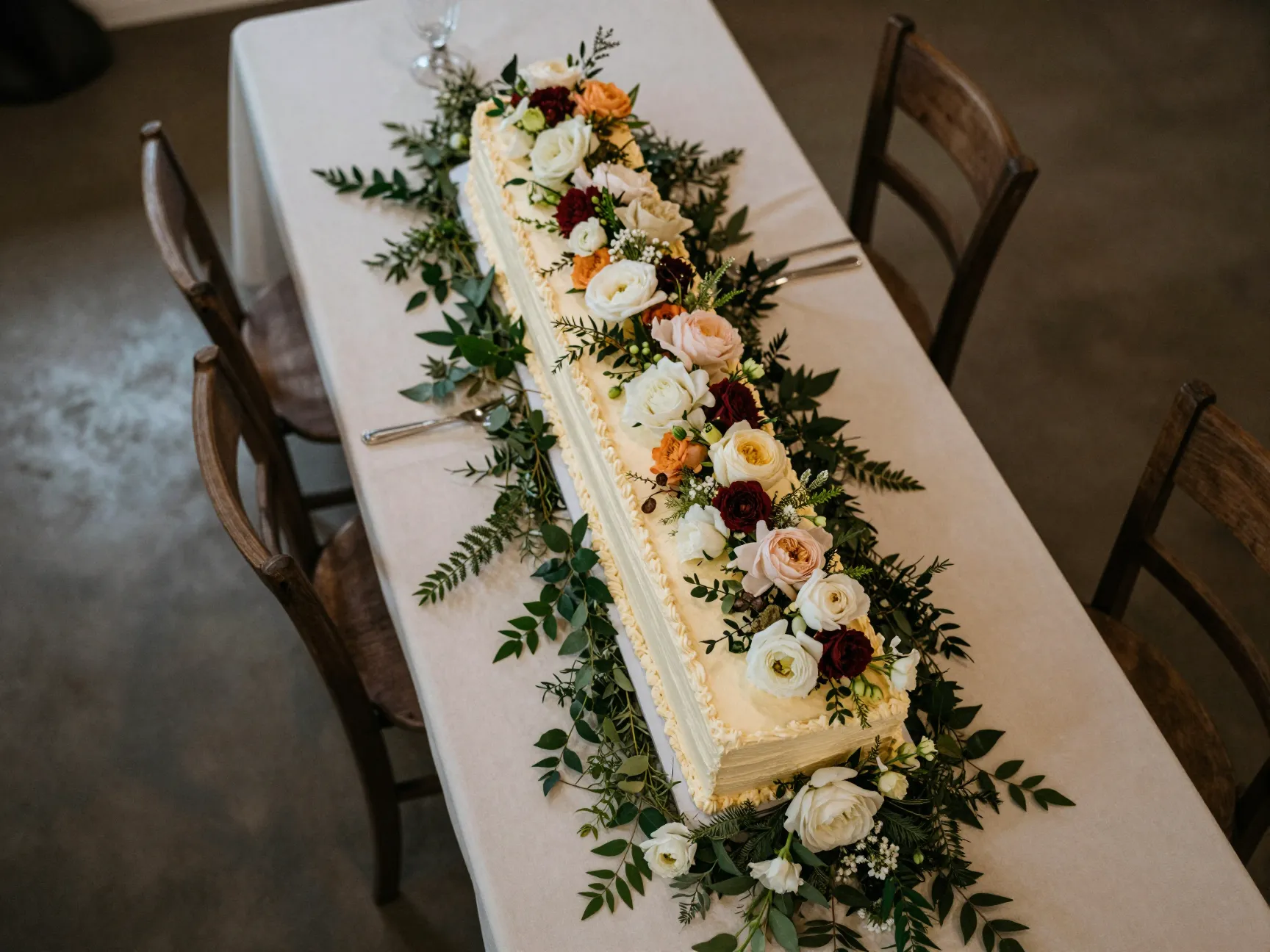 Long rectangular wedding cake with cascading flowers on table