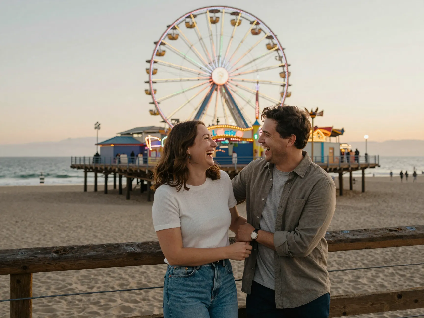An engaged couple laughs under the ferris wheel on santa monica pier