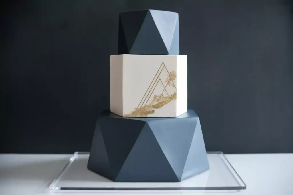 Three-tiered geometric cake with dark blue and white layers, gold line art on the middle tier.