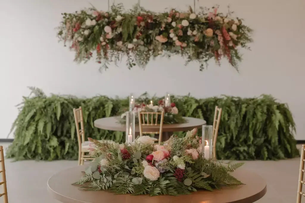 Round tables with floral centerpieces, gold chairs, and lush greenery decorations in a bright room.