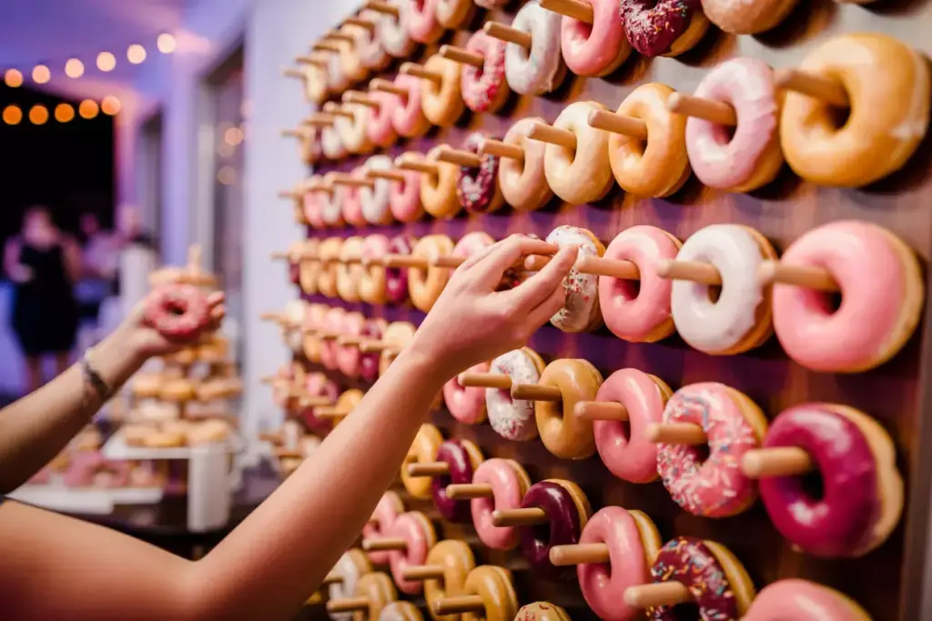 Person picking a donut from a wall display of assorted donuts arranged on wooden pegs at an event.