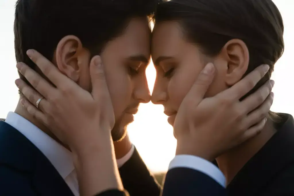 A couple gently touch foreheads, holding each others faces tenderly at sunset.