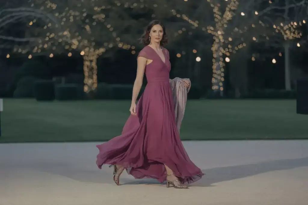 Woman in a flowing magenta gown walks outdoors at night, with trees decorated with string lights in the background.