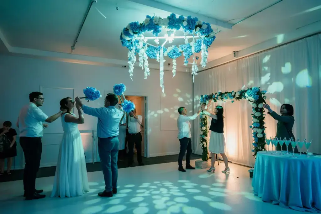 People participate in a wedding celebration under blue floral decorations and soft, patterned lighting.