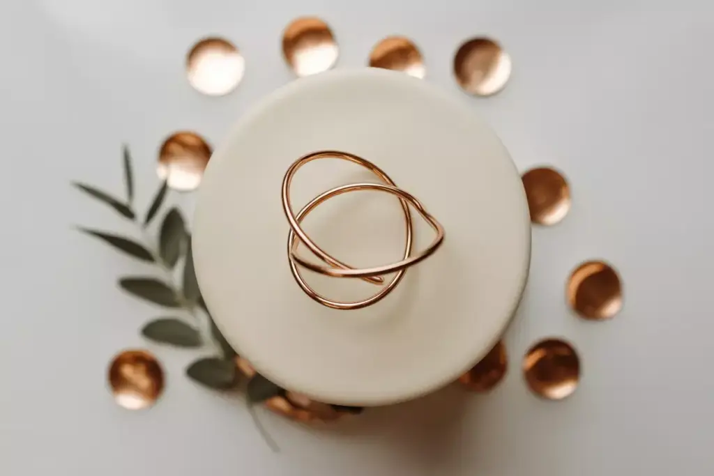 Gold rings on a white surface, surrounded by green leaves and copper circles, viewed from above.