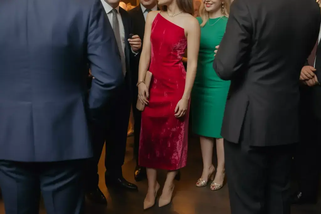 People in formal attire gather at an indoor event, with a woman in a red dress in the center.