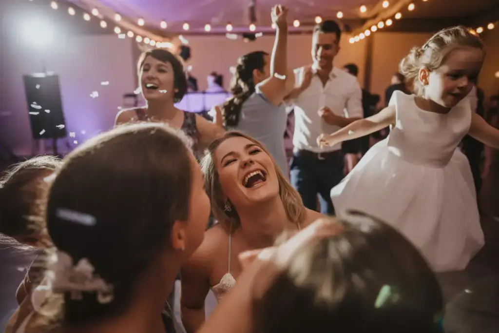 A group of people laugh and dance at a festive indoor party with string lights overhead.
