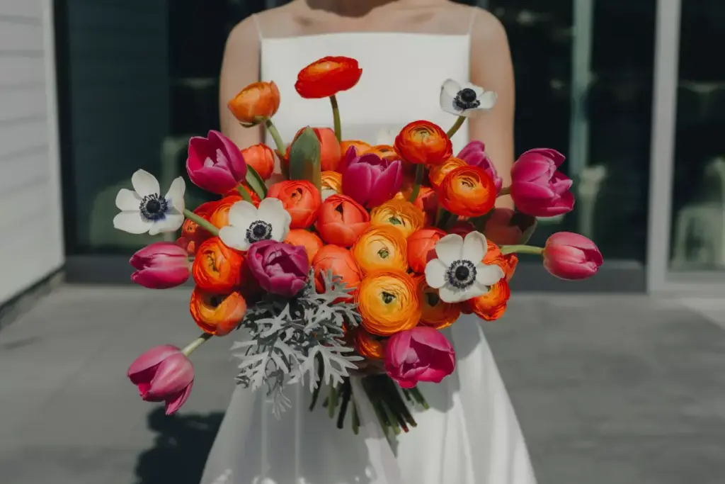 Bride in a white dress holding a colorful bouquet of pink, orange, and white flowers.