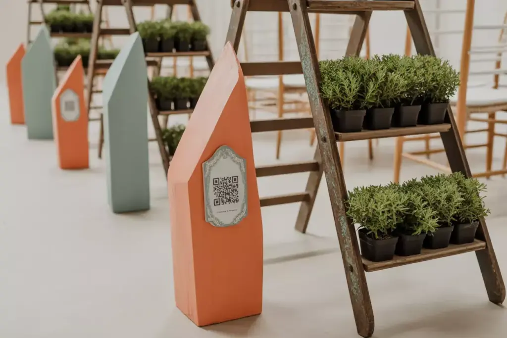 Small potted plants on wooden ladders next to colorful house-shaped stands with QR codes.