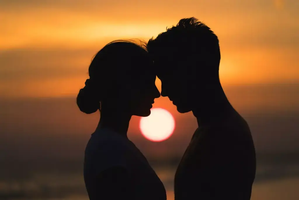 Silhouetted couple touching foreheads at sunset with the sun low on the horizon.