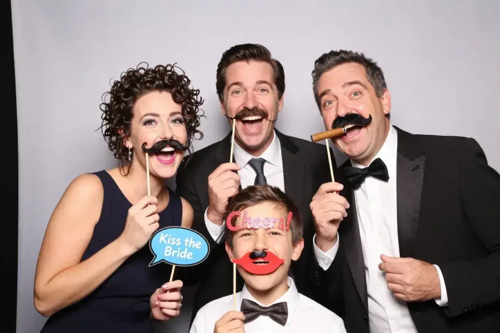 Group of guests posing with mustache and lip props at wedding photo booth