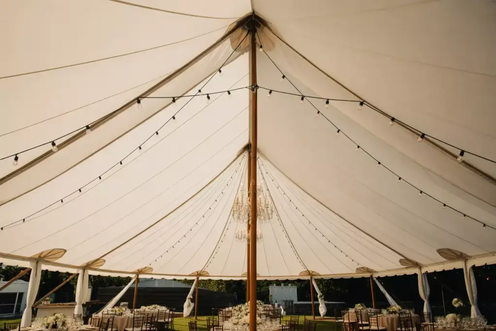 Classic white pole tent with chandelier and fabric draping under evening sky