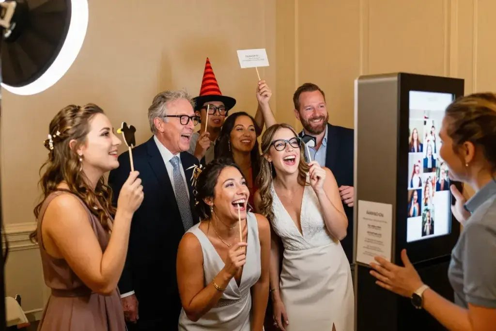 Multi generational guests laughing with attendant at wedding selfie booth
