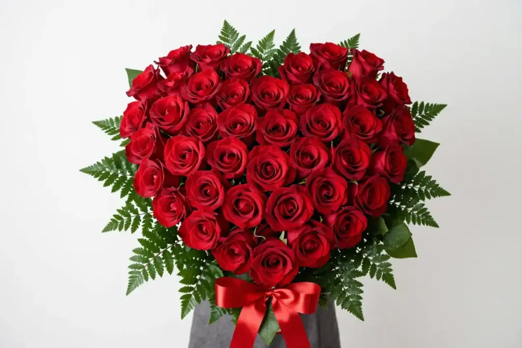 Symmetrical dense heart shaped bouquet of red roses on foliage