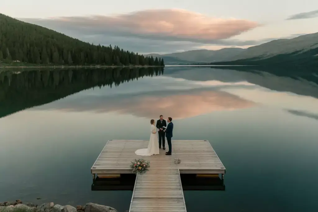 Intimate lakeside dock ceremony with calm water and sunset reflection