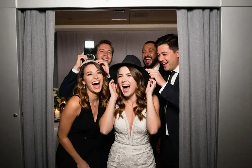 Guests sharing genuine laughter inside wedding photo booth candid