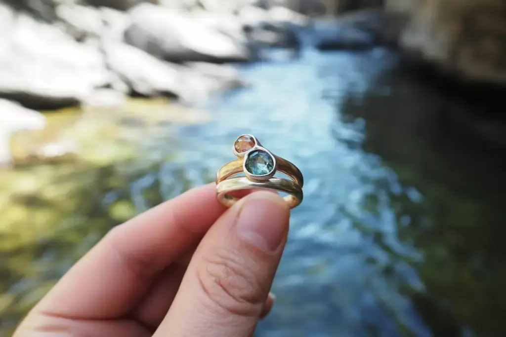 Raw teal sapphire in organic setting held over mountain stream