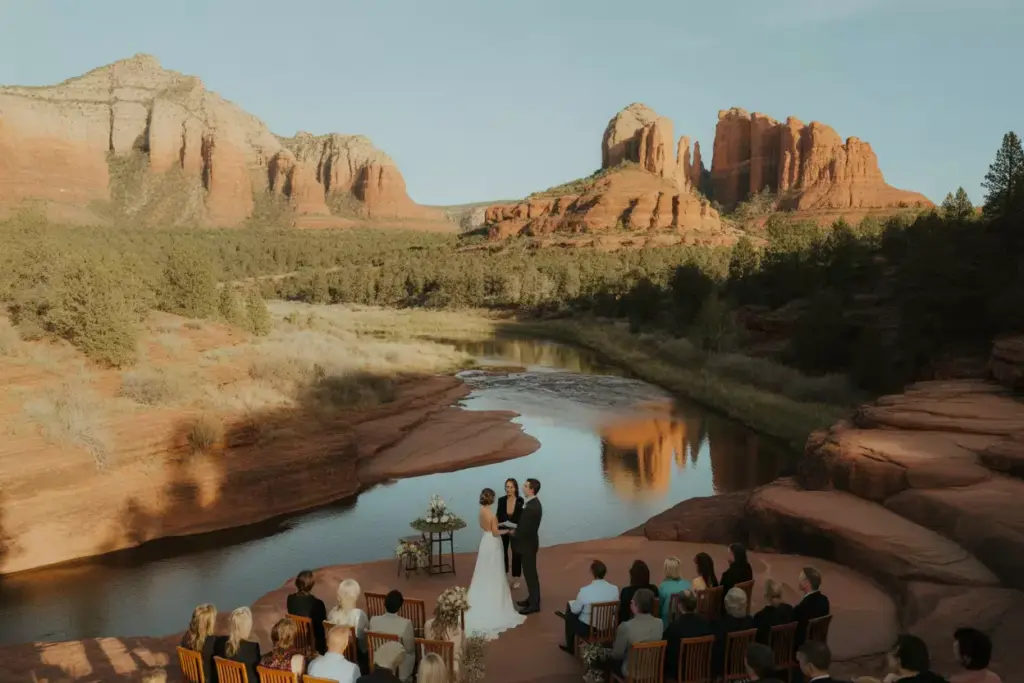 Couple exchanging vows on terrace overlooking creek with red rocks
