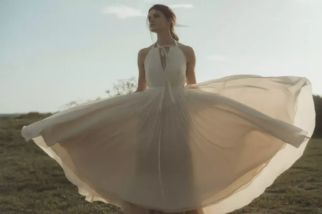 Bride in chiffon halter dress walking on beach at sunset